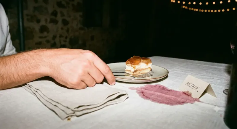 Une part de gâteau, une tache de vin sur la nappe et un marque-place au nom d’Arthur.