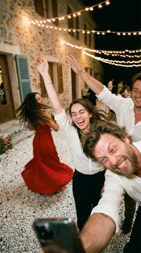 Un selfie pris sur la piste, bras levés et rires, une invitée en robe rouge tourne derrière.