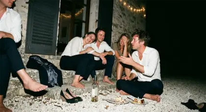 Quatre invités assis pieds nus sur les marches, une bouteille et des assiettes de gâteau posées au sol.